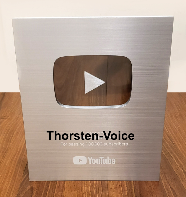 Zeigt eine Fotomontage mit dem silbernen Youtube Play Button für 100000 Abonnenten, mit dem Schriftzug "Thorsten-Voice" als Motivation diese Zahl an Abos zu erreichen.